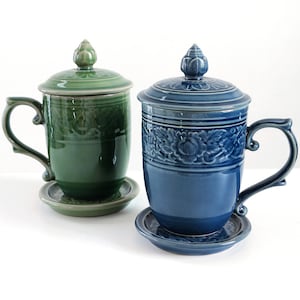 Puede incluir: Dos tazas de té de cerámica con tapas y platillos a juego. La taza de té de la izquierda es verde con un diseño floral y la taza de té de la derecha es azul con un diseño floral.