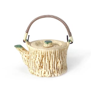 May include: A ceramic teapot with a tree trunk design. The teapot is beige with brown vertical lines, a green-tipped spout, and a lid with a green knob. It has a woven handle with brown and white stripes.