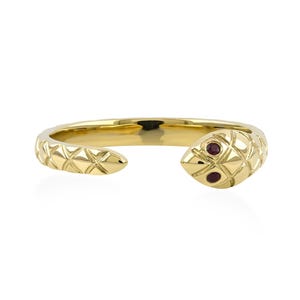 Può includere: Un anello color oro a forma di serpente. La testa del serpente presenta due piccole gemme rosse per gli occhi. L'anello ha un motivo strutturato a scaglie e un design aperto.