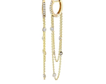May include: A pair of gold hoop earrings featuring a hinged closure and multiple delicate gold chains hanging from the bottom. Each chain is accented with small, round, clear stones set in gold, creating a layered, dangling effect.
