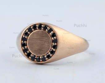 May include: A gold signet ring with a black onyx stone set in a circle around the center of the ring.