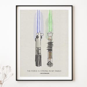 May include: A black framed print with a white background featuring a drawing of two lightsabers, one blue and one green. The text "The Force is strong in my family. - Luke Skywalker" is printed below the lightsabers.