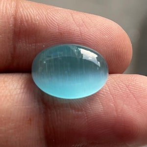 May include: A light blue oval cabochon gemstone with a smooth, polished surface.