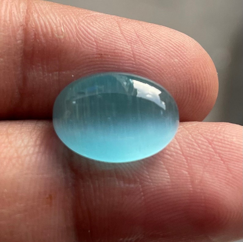 May include: A light blue oval cabochon gemstone with a smooth, polished surface.