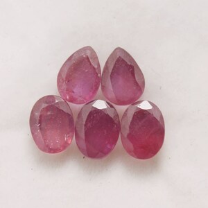 May include: Five pear-shaped pink gemstones, likely rubies, with faceted surfaces.