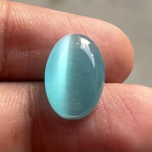 May include: A light blue oval cabochon gemstone with a chatoyant effect. The stone has a smooth, polished surface.