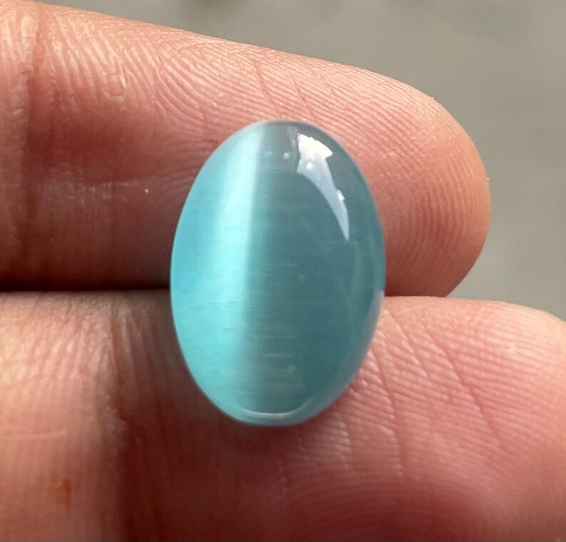 May include: A light blue oval cabochon gemstone with a chatoyant effect. The stone has a smooth, polished surface.