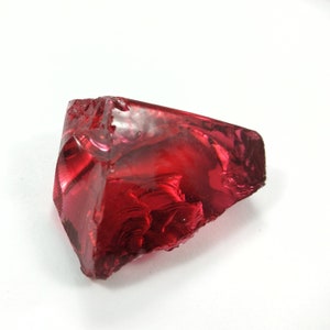 May include: A large, deep red, faceted crystal with a rough, irregular shape. The crystal is translucent and has a slight shimmer.