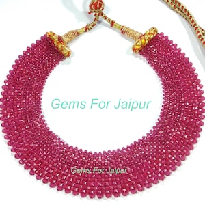 May include: A pink crystal bead necklace with a gold and red tassel closure. The necklace is made of many strands of beads and is a beautiful statement piece. "Gems For Jaipur" is written on the image.