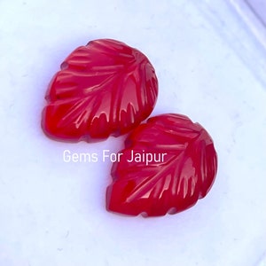 Op de afbeelding: Twee rode, bladvormige cabochons van edelsteen. De cabochons zijn gesneden met een bladontwerp en hebben een glanzende afwerking.
