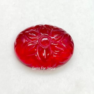 May include: A red gemstone carved with a flower design. The gemstone is oval shaped and has a glossy finish.