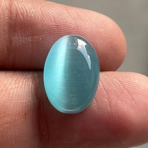 May include: A light blue oval cabochon gemstone with a chatoyant effect. The stone is smooth and polished.