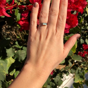May include: A gold ring with a light blue rectangular gemstone. The ring is on a person's finger.