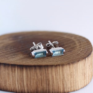 May include: A pair of silver stud earrings with light blue rectangular gemstones.