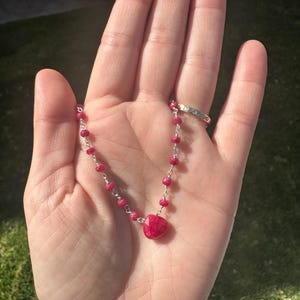 May include: A silver chain necklace with small red beads and a larger red gemstone pendant.