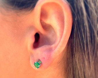 Puede incluir: Primer plano de una oreja con un pequeño pendiente de piedra preciosa verde.