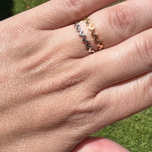 Peut inclure: Deux bagues en or et en argent avec un motif en zigzag. Les bagues sont empilées sur un doigt.