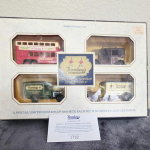 May include: A boxed set of Hamleys toy vehicles, including a red double-decker bus, a dark brown carriage, and two green delivery trucks. The box reads "Made in England" and "Hamleys, the finest toyshop in the world."