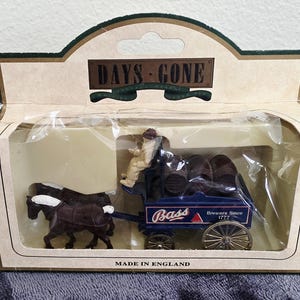 May include: A miniature model of a blue Bass Brewery wagon pulled by two brown horses. The wagon carries barrels and a figure. The packaging reads "DAYS GONE" and "MADE IN ENGLAND".