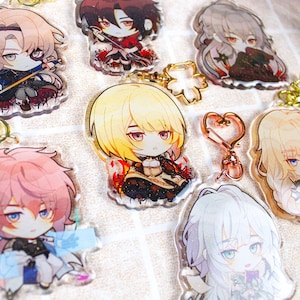 Könnte beinhalten: Ein Set aus zehn bunten Anime-Charakter-Acryl-Anhängern. Jeder Anhänger zeigt einen anderen Charakter mit einzigartigen Haar- und Kleidungsstilen. Die Anhänger sind an Schlüsselanhängern befestigt.