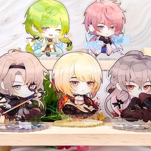 Op de afbeelding: Vijf acryl anime-karakterfiguren. Elke figuur heeft een unieke haarstijl en outfit, staand op een heldere basis. Ze worden tentoongesteld op een houten plank. De karakters hebben gedetailleerde gelaatstrekken.