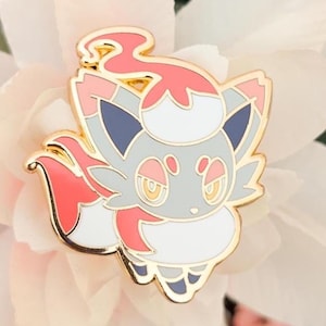 Könnte beinhalten: Ein farbenfroher Emaille-Pin mit einem cartoonartigen, fuchsähnlichen Charakter mit goldenen Konturen. Der Pin hat einen grauen Körper, weiße Akzente und rote und blaue Details. Der Pin ist auf einer weißen Blume platziert.