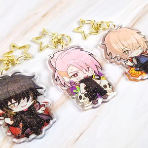 Puede incluir: Tres llaveros acrílicos de estilo anime con cierres dorados en forma de estrella. Cada llavero presenta un personaje diferente con colores de cabello y atuendos únicos. Los personajes están sobre un fondo blanco.
