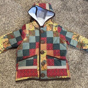 May include: A quilted jacket with a hood, featuring a patchwork design of various colors and patterns, including red, green, yellow, and brown. The jacket has a button closure and two pockets.
