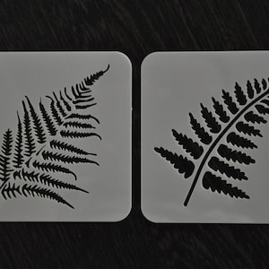 May include: Two white plastic stencils with fern leaf designs. The stencils are approximately 4 inches by 4 inches.