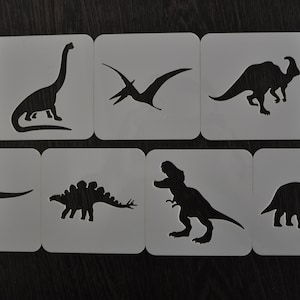May include: Set of six white plastic stencils featuring different dinosaur silhouettes. The stencils are perfect for crafting and decorating projects.