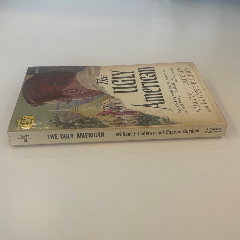May include: A vintage paperback book titled "The Ugly American" by William J. Lederer and Eugene Burdick. The cover features a portrait of a man and a landscape scene. The book is a Crest Book.