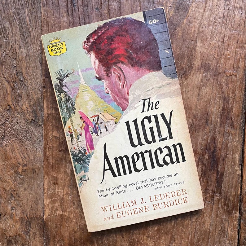 May include: Vintage paperback book titled "The Ugly American" with a cover illustration of a man and a colorful scene. The book is a Crest Book edition and includes text from the New York Times.