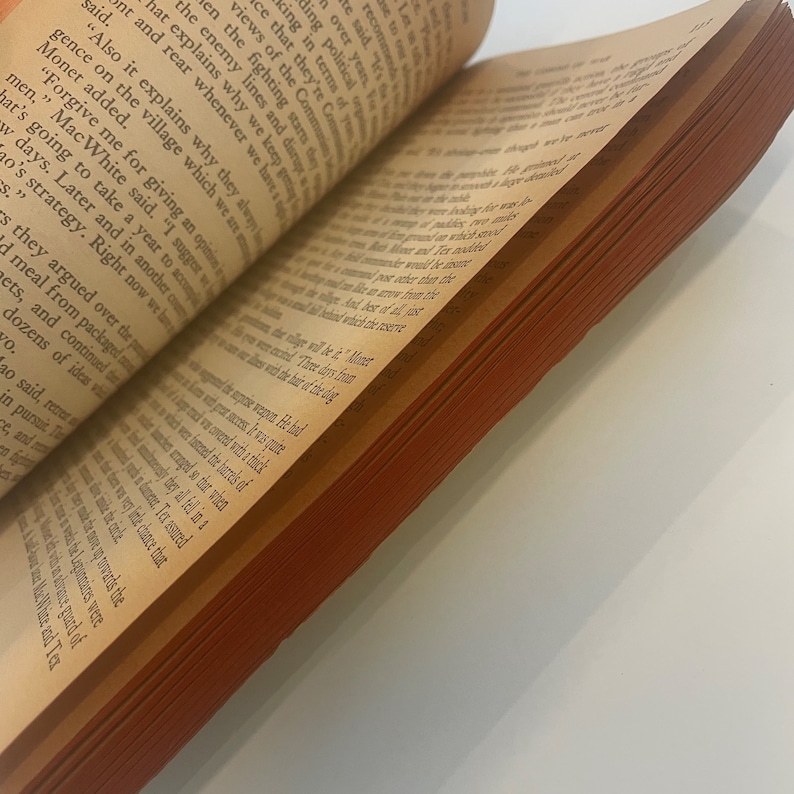 May include: An open book with aged, yellowed pages and a reddish-brown edge. The text is in black, with the pages slightly curved. The book is angled, showing the text and the side of the pages.