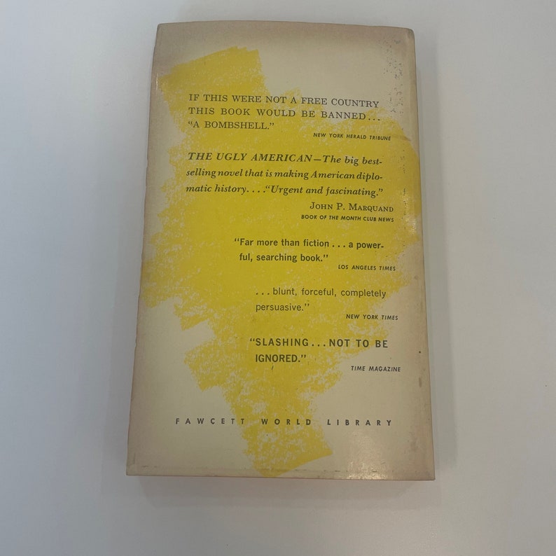 May include: The back cover of "The Ugly American" book. The cover is off-white with yellow accents. Text includes quotes from various publications and the Fawcett World Library logo. The book's title is prominently displayed.