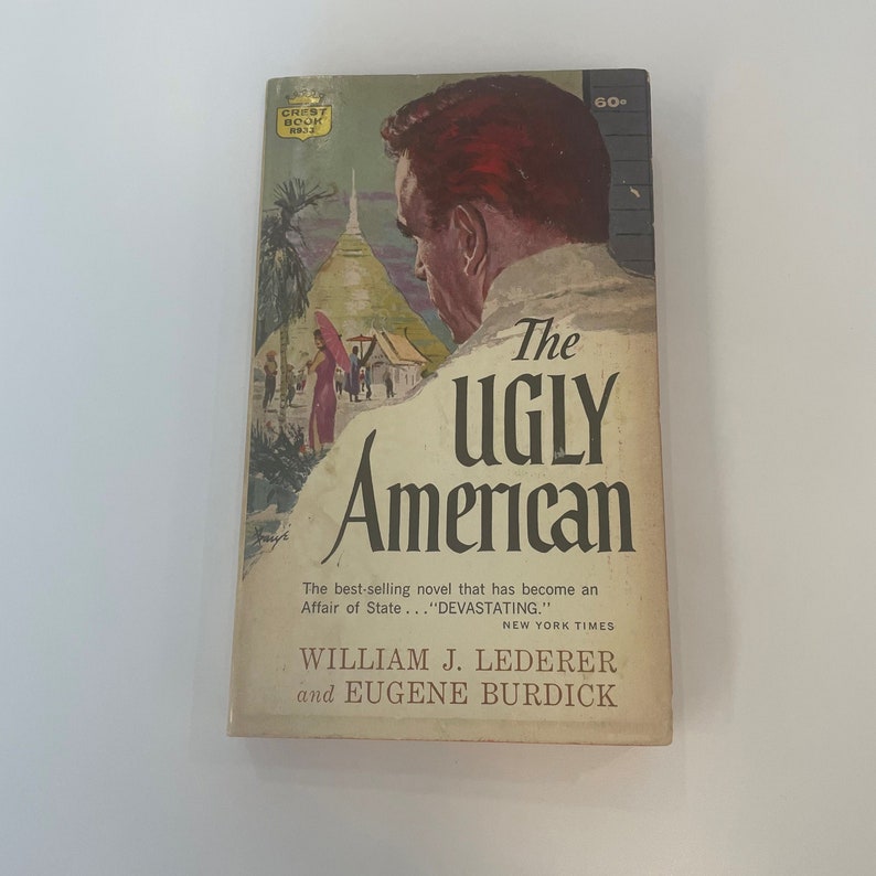 May include: Vintage paperback book titled "The Ugly American." The cover features an illustration of a man with red hair and a white shirt, with a background of a pagoda and figures. The book is by William J. Lederer and Eugene Burdick.