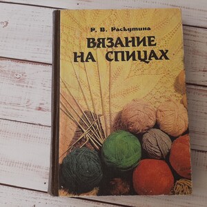 Puede incluir: Un libro de tapa dura titulado Viazanie na spitsakh de R. V. Raskutina con una cubierta amarilla que presenta una ilustración de varias bolas de lana coloridas en tonos verde, rojo, marrón y beige, junto con un juego de agujas de tejer.