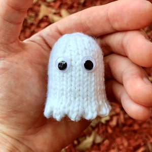 Könnte beinhalten: Ein weißer gestrickter Geist mit Glitz Augen. Der Geist wird in einer Hand gehalten.