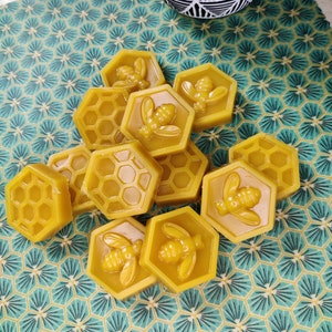 Puede incluir: Primer plano de un grupo de envoltorios de cera de abeja amarilla con un patrón de panal y un diseño de abeja. Los envoltorios están sobre una superficie con un patrón verde y blanco.