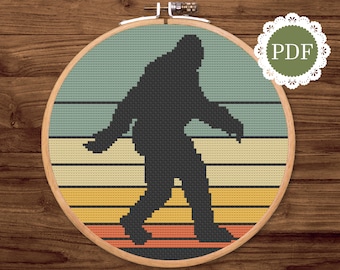 May include: A cross-stitch pattern featuring a silhouette of Bigfoot walking across a retro-style sunset with orange, yellow, and blue stripes. The pattern is in a circular embroidery hoop.