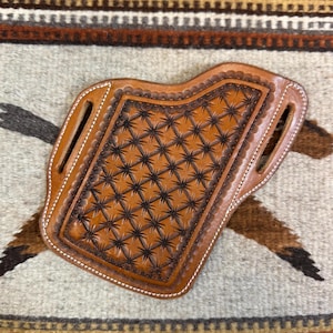 May include: A brown leather holster with a star-shaped pattern and white stitching. The holster is designed to hold a firearm.