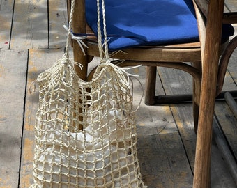 May include: A white crocheted net bag hanging on a wooden chair. The bag is empty and has a rope handle.