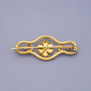 Puede incluir: Broche dorado con dise&ntilde;o floral. El broche presenta una flor central y est&aacute; enmarcado por un borde decorativo y curvado. El alfiler es un accesorio cl&aacute;sico.