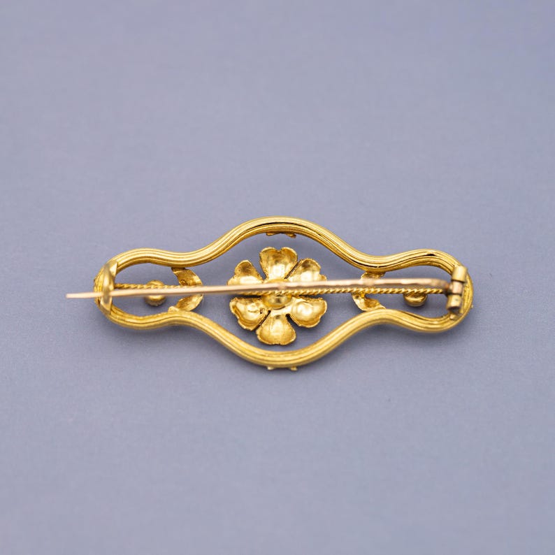 Puede incluir: Broche dorado con dise&ntilde;o floral. El broche presenta una flor central y est&aacute; enmarcado por un borde decorativo y curvado. El alfiler es un accesorio cl&aacute;sico.
