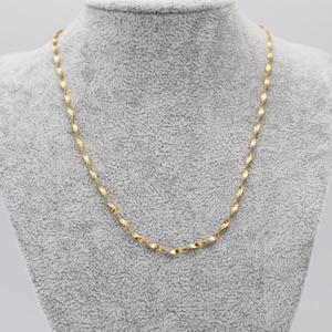 May include: A delicate gold-colored necklace with a twisted rope design. The necklace is displayed on a gray mannequin bust. The chain is made of small, repeating, twisted links that catch the light.