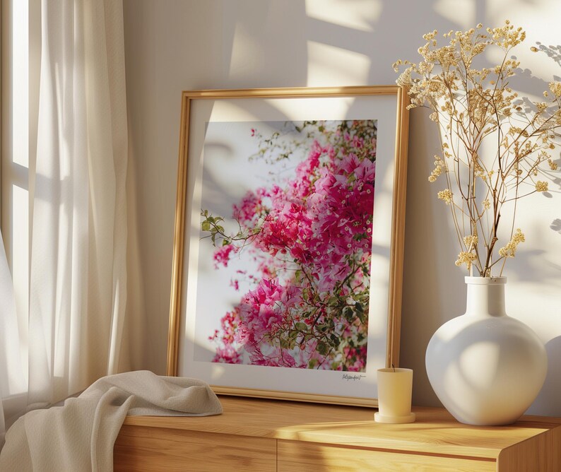 May include: A framed print of a pink flower arrangement with a white background. The frame is gold and the print is hanging on a wall.