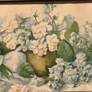 May include: A framed floral still life painting. The artwork features a vase filled with white flowers and green leaves. The vase is a muted green color. The background is a soft, neutral tone. The frame is black.