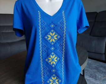 Peut inclure: Un t-shirt bleu avec un motif brodé jaune et bleu sur le devant. Le motif présente un motif géométrique avec des fleurs.