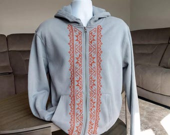 Peut inclure: Un sweat à capuche gris clair avec une fermeture éclair et un motif brodé orange sur le devant.