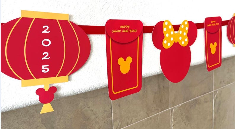 Puede incluir: Bandera roja y amarilla del A&ntilde;o Nuevo Chino con linternas rojas, sobres rojos y una cabeza de Mickey Mouse con un lazo amarillo. Las linternas tienen el a&ntilde;o 2025 impreso en ellas. Los sobres rojos tienen el texto "&iexcl;Feliz A&ntilde;o Nuevo Lunar!" impreso en ellos.