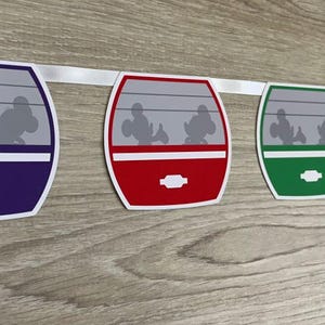 May include: A colourful garland featuring five purple, red, green, orange, and blue paper cutouts of a Disney monorail car with Mickey Mouse and friends silhouettes inside.